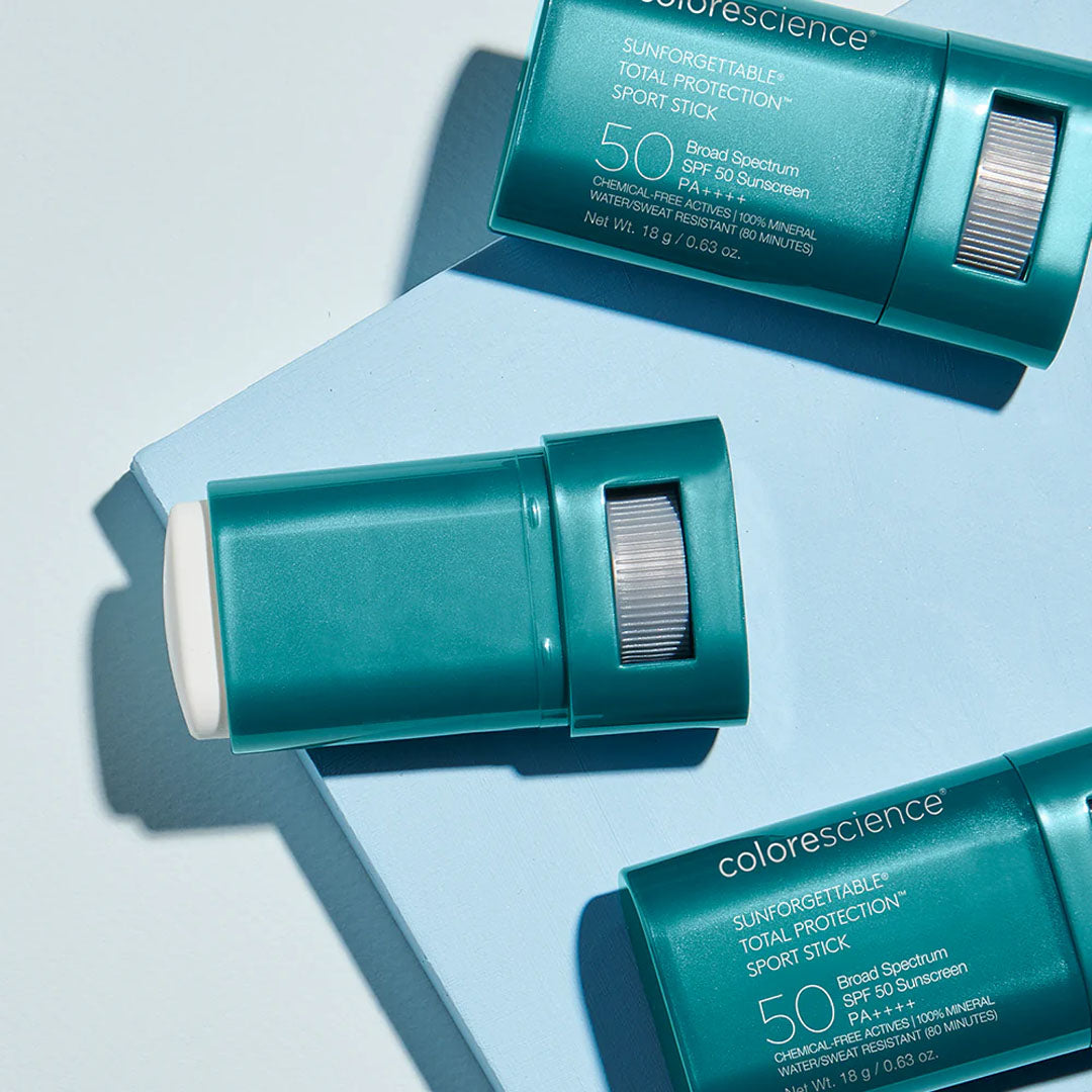 Teal Colorescience SPF 50 mineral sunscreen sticks with twist-up applicators arranged on a light blue surface.