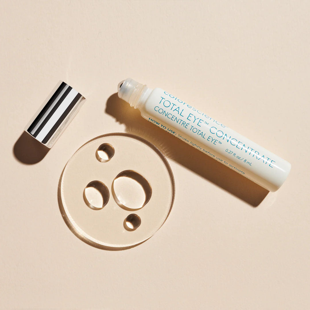 Colorescience Total Eye Concentrate rollerball serum with a striped cap next to clear serum droplets on a beige background.