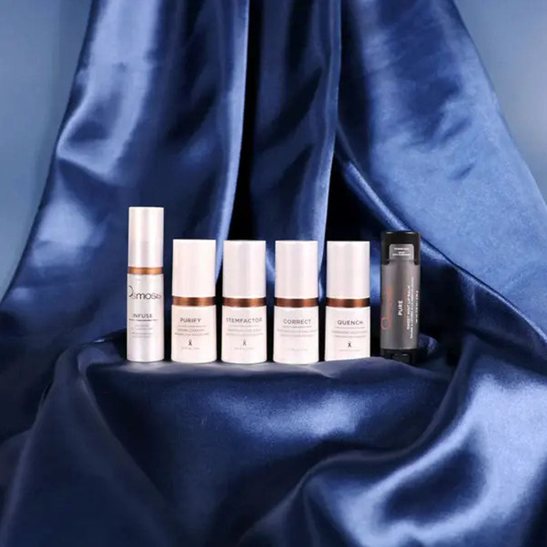 Five white and one black Osmosis Lunar Travel Kit skincare bottles on a draped blue satin background.