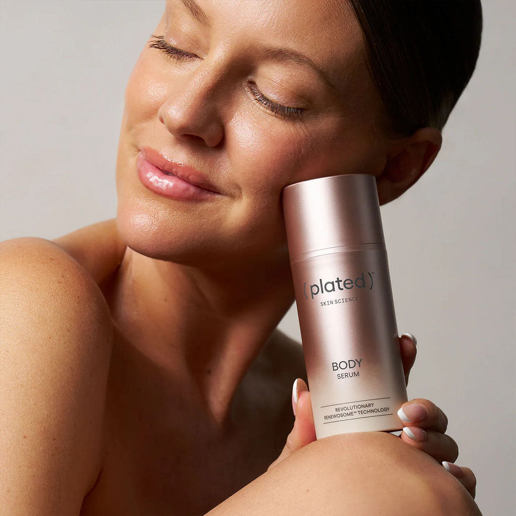 Woman holding a 'plated' body serum bottle against a neutral background