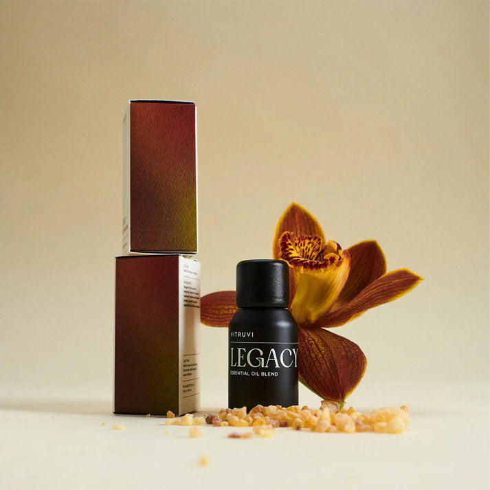 Vitruvi Legacy essential oil blend in a black bottle with its box, frankincense resin, and an orange orchid.