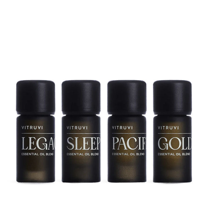 Four dark amber glass Vitruvi essential oil blend bottles with black caps, labeled Legacy, Sleep, Pacific, and Gold.